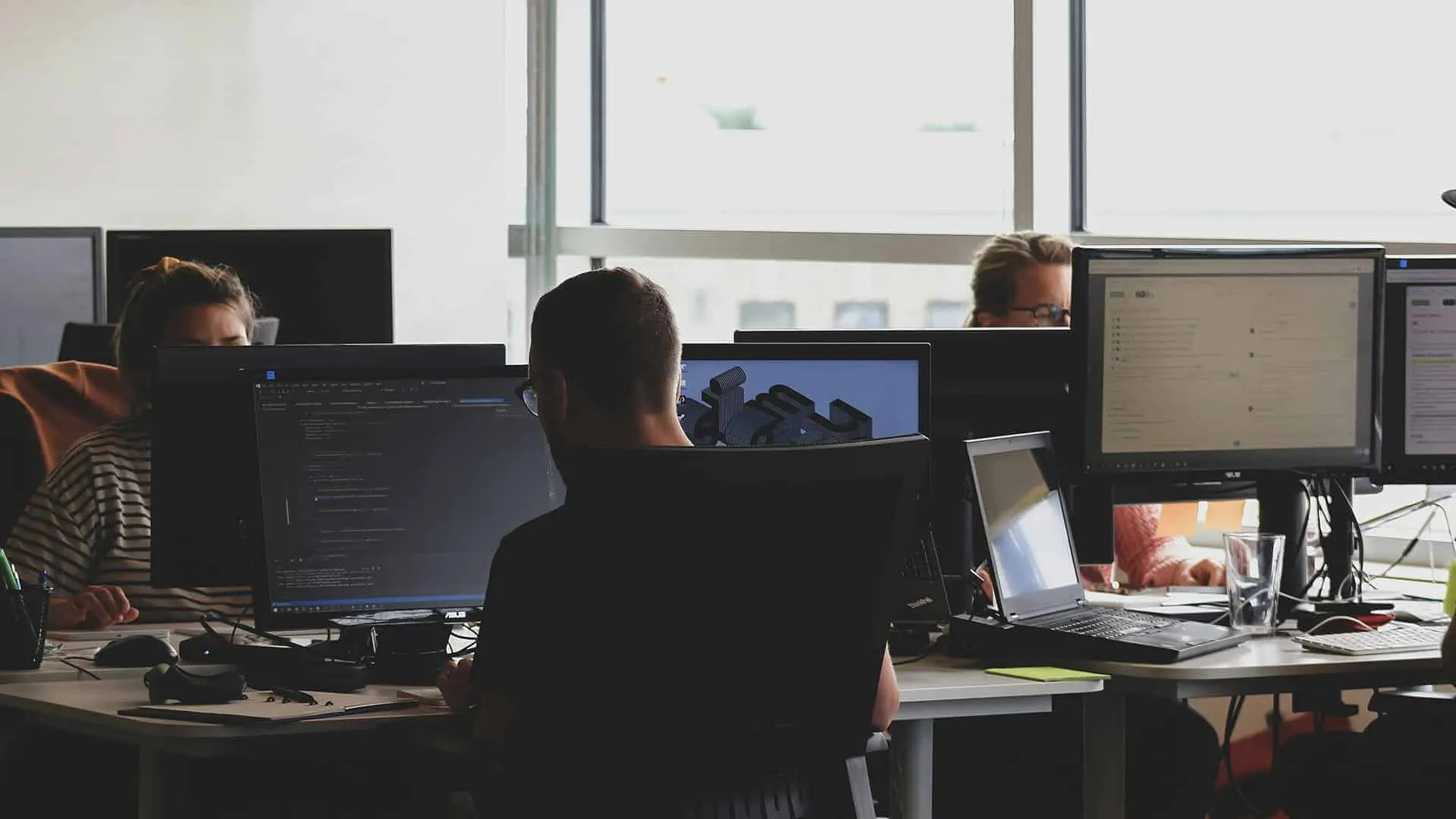 Personas trabajando frente a computadoras en una oficina moderna.